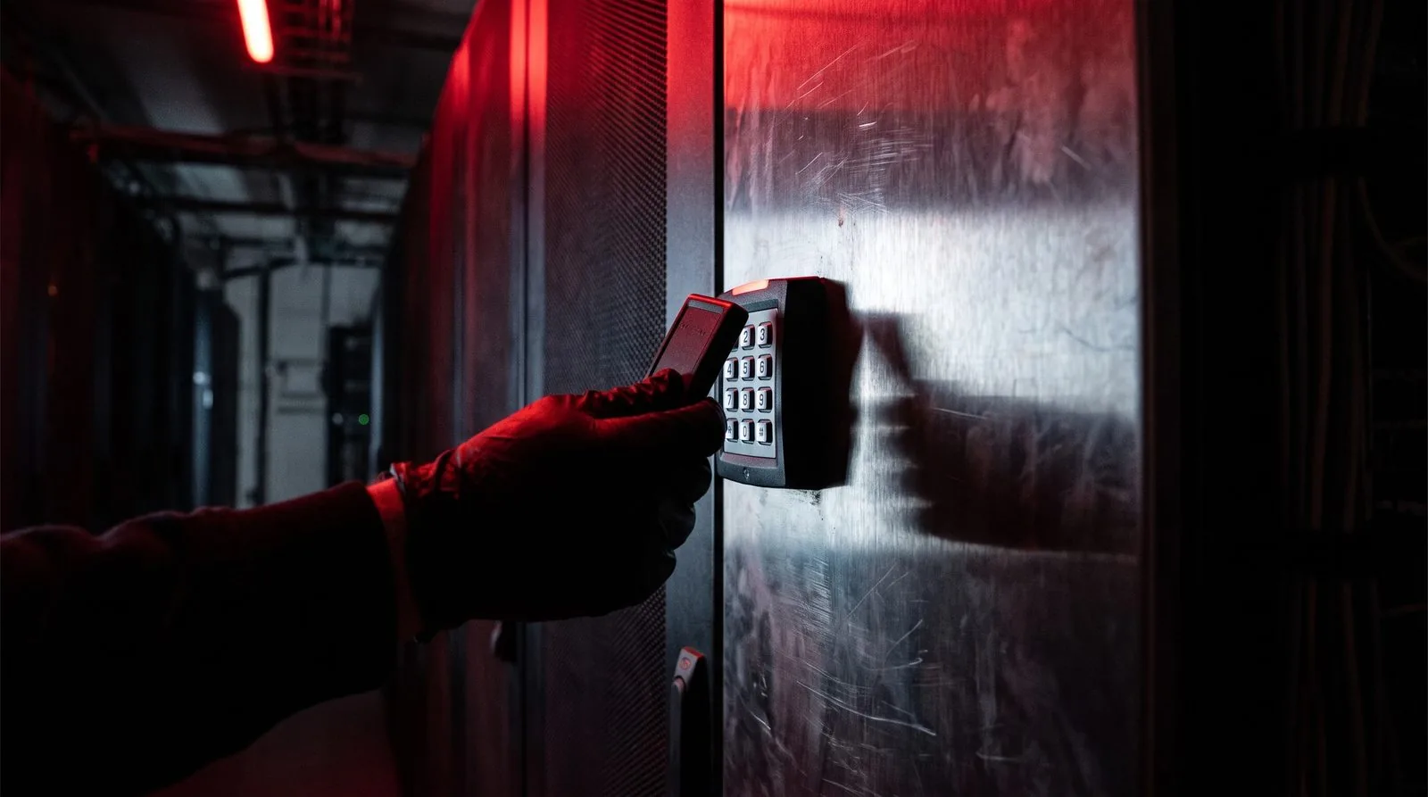 Gloved hand holding an RFID cloning device against a keypad on a server cabinet door